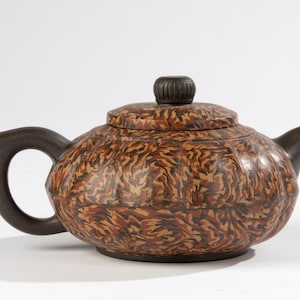 Peut inclure: Une théière ronde en céramique brune et noire avec un motif. Le couvercle de la théière a un bouton sur le dessus.