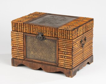 May include: A rectangular wooden chest featuring a bamboo-style exterior with brass accents. The front panel displays an embossed metallic plate with a floral pattern, while the lid has a dark leather-like inlay. It sits on a scalloped base.