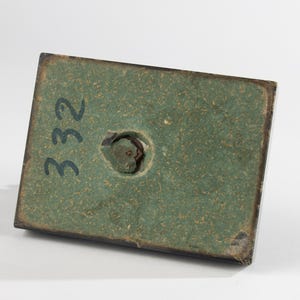May include: A rectangular base with a green textured surface and a dark border. The number "332" is written in black on the surface. A circular hole is visible near the centre.