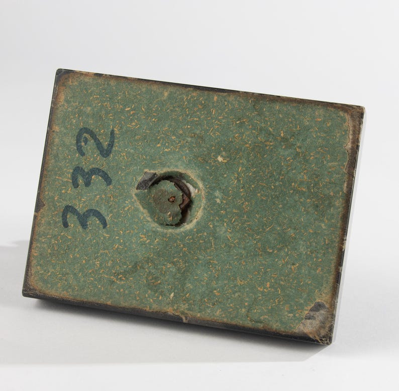 May include: A rectangular base with a green textured surface and a dark border. The number "332" is written in black on the surface. A circular hole is visible near the centre.