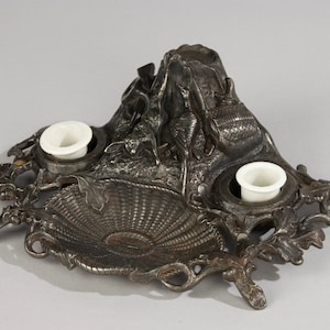 Pode incluir: Um tinteiro de ferro fundido com um design decorativo que apresenta um toco de árvore e folhas. O tinteiro tem dois tinteiros de porcelana branca e um poço central para uma pena.