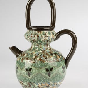 May include: A ceramic teapot featuring a glossy dark brown handle and base. The body displays a complex mosaic pattern of green, brown, and blue geometric shapes, with a central horizontal band containing repeating dark star-like motifs.