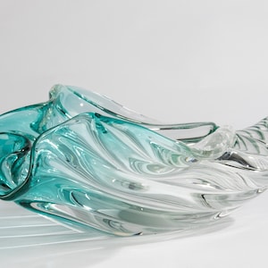 May include: A clear glass bowl with a teal blue swirl design. The bowl is shaped like a seashell and has a wavy, organic form.