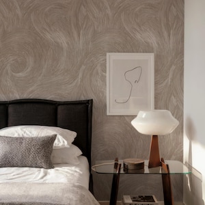 Peut inclure: Intérieur de chambre avec un lit aux draps blancs, une couverture grise et un coussin texturé. Une table de chevet en verre supporte une lampe à abat-jour blanc et socle en bois, des livres et un objet décoratif. Le mur présente un motif tourbillonnant.