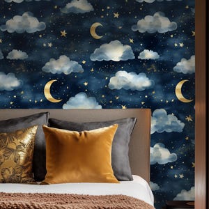 May include: A bedroom with a navy blue wallpaper featuring a repeating pattern of white clouds, gold stars, and crescent moons. The wallpaper is behind a bed with a brown knitted throw blanket and gold and gray pillows.