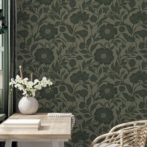 May include: A green floral wallpaper with a repeating pattern of dark green leaves and flowers. The wallpaper is shown in a room with a white desk and a wicker chair.