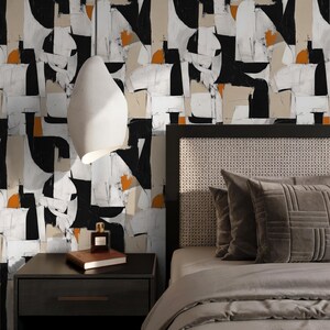 May include: A bedroom scene featuring a modern aesthetic. The focal point is a bed with a gray comforter and pillows. The headboard has a woven design. The wall behind the bed is adorned with abstract art in black, white, beige, and orange. A nightstand with a lamp and a book is on the left.