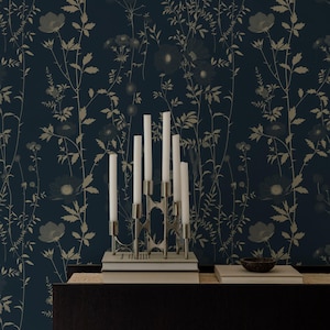 May include: A dark blue floral wallpaper with a silver candelabra holding white candles. The wallpaper features a repeating pattern of flowers and foliage in shades of beige and gray. A dark wooden surface is below.