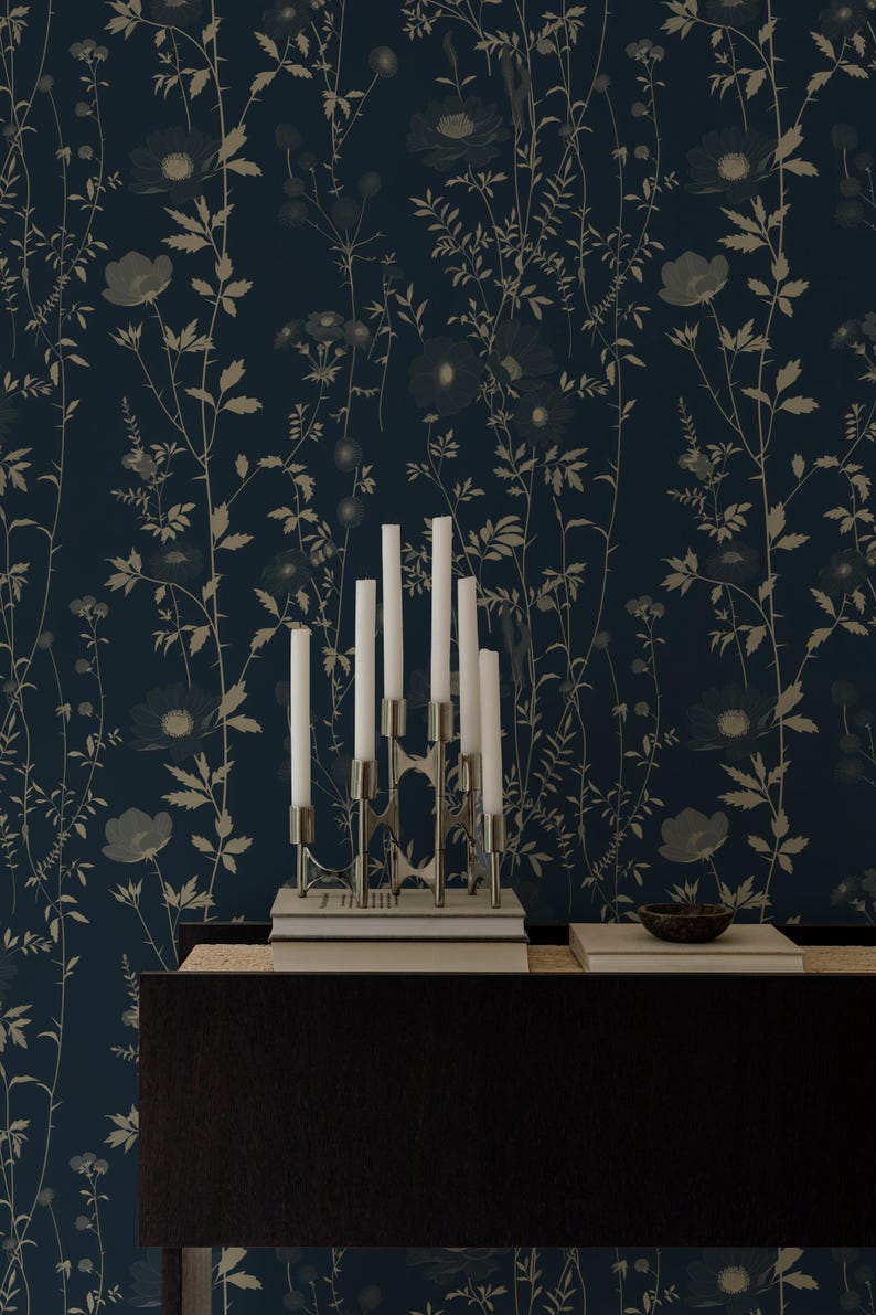 May include: A dark blue floral wallpaper with a silver candelabra holding white candles. The wallpaper features a repeating pattern of flowers and foliage in shades of beige and gray. A dark wooden surface is below.