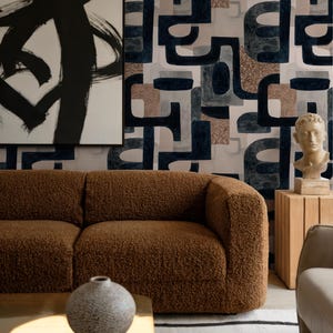 Pode incluir: Uma sala de estar moderna com um sofá castanho texturizado, uma mesa de centro dourada e um tapete estampado. O fundo inclui arte abstrata e uma parede com um design geométrico em tons de azul, castanho e cinzento.