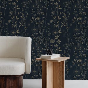 May include: Dark navy wallpaper with a botanical design featuring beige-colored flowers and foliage. A white armchair with a wooden base and a small wooden side table with a book and decorative object are in the foreground.
