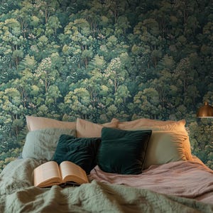 May include: A bedroom scene featuring a forest-themed wallpaper in shades of green. The bed is made with a green comforter, pillows, and a book. A gold-colored lamp is visible on the right side of the image.