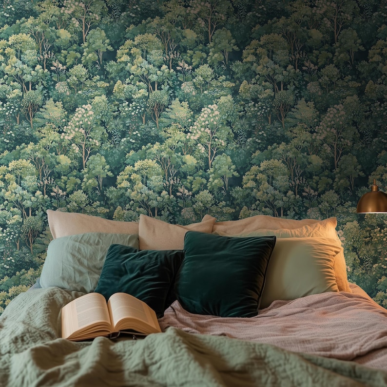 May include: A bedroom scene featuring a forest-themed wallpaper in shades of green. The bed is made with a green comforter, pillows, and a book. A gold-colored lamp is visible on the right side of the image.