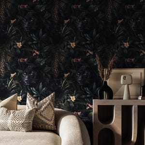 Puede incluir: Un interior de sala de estar con un sof&aacute; y una mesa auxiliar. La pared est&aacute; cubierta con papel tapiz verde oscuro con un patr&oacute;n repetitivo de jaguares negros e estampado de leopardo dorado. El sof&aacute; est&aacute; tapizado en tela beige claro y tiene dos cojines con un patr&oacute;n geom&eacute;trico. La mesa auxiliar est&aacute; hecha de madera y tiene un dise&ntilde;o &uacute;nico con estantes abiertos.