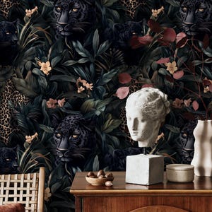 Puede incluir: Un papel tapiz verde oscuro y negro con un tema de jungla. El papel tapiz presenta panteras negras, estampado de leopardo y plantas tropicales. Un busto de yeso blanco de una mujer est&aacute; en primer plano.