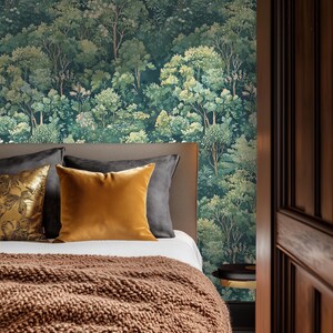 May include: A bedroom scene featuring a bed with a brown knitted blanket and pillows in gold and gray tones. The headboard is against a wall with a forest mural in shades of green. A dark wooden door frame is visible on the right.