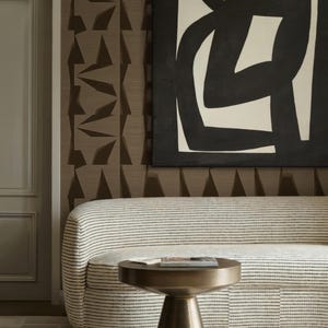 Peut inclure: Un salon moderne avec un canapé rayé, une table d'appoint en laiton et une œuvre d'art abstraite. Le canapé a un design incurvé et est recouvert d'un tissu à fines rayures foncées. La table d'appoint a un plateau rond et une base conique.