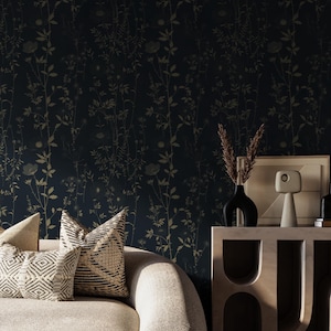 May include: A dark blue floral wallpaper with a repeating pattern of gold-colored flowers and foliage. Two decorative pillows with geometric patterns rest on a light-colored sofa. A black vase and a framed picture sit on a wooden table.