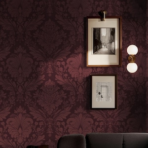 May include: A burgundy wall with a damask pattern. Two framed black and white pictures hang on the wall, along with a brass and white globe light fixture. A dark gray sofa is visible at the bottom.