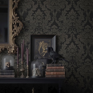 May include: A gothic-themed display featuring a black raven perched on antique books. The scene includes a skull in a glass dome, candles, and a framed artwork with a gold design, all set against a dark floral wallpaper.