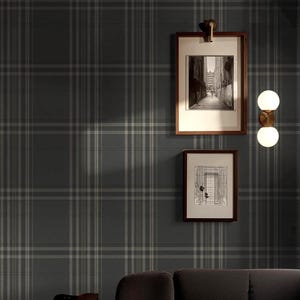 May include: Dark gray wallpaper featuring a subtle, repeating plaid pattern with thin, lighter gray vertical and horizontal lines. The wall is decorated with two framed black and white prints and a vertical wall sconce with two round white glass globes.