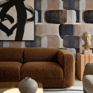 Pode incluir: Uma sala de estar moderna com um sofá castanho texturizado, uma mesa de centro dourada e um tapete estampado. A sala também inclui uma grande pintura abstrata e um vaso decorativo. O papel de parede tem um padrão repetitivo de formas arredondadas.