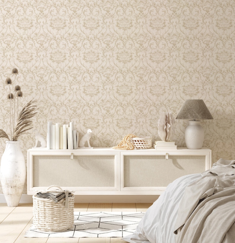 May include: A white dresser with two drawers and a white lamp with a gray lampshade. The dresser is against a wall with a beige damask wallpaper. There is a white rug with a geometric pattern on the floor.