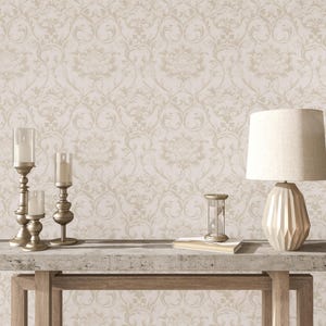 May include: A beige damask wallpaper with a subtle embossed texture. A wooden table with a concrete top features three gold candle holders and a gold lamp with a white shade. An hourglass sits on the table.
