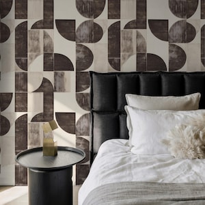 Puede incluir: Interior de dormitorio con cabecero negro, ropa de cama blanca y una pequeña mesita de noche negra. La pared está adornada con un patrón geométrico en tonos marrones y beige. Un objeto decorativo dorado está sobre la mesita de noche.