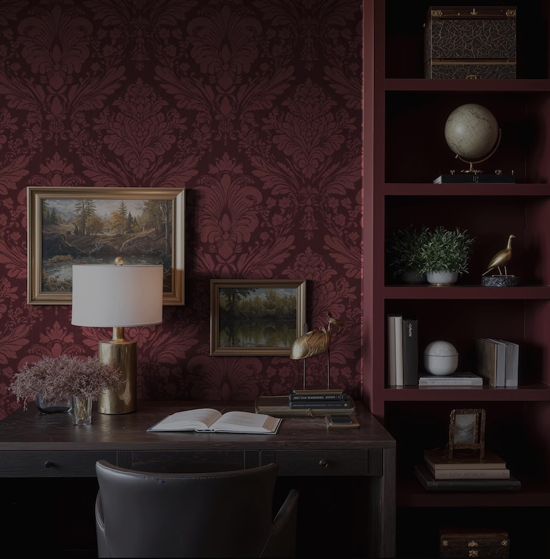 May include: A home office with a dark wood desk, a leather chair, and a burgundy damask wallpaper. The desk has a lamp, artwork, and decorative items. A built-in bookshelf displays books, a globe, and a decorative bird.
