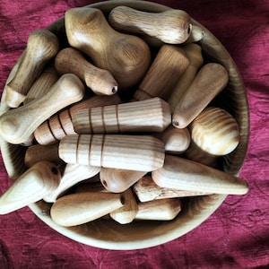 May include: A wooden bowl filled with a variety of wooden knobs and handles. The knobs and handles are all different shapes and sizes, and they are made of a light brown wood.