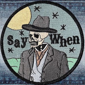 May include: A round embroidered patch with a skeleton wearing a hat and a suit. The background is a night sky with a moon and stars. The text "Say When" is embroidered on the patch.