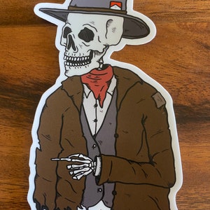 May include: A sticker featuring a skeleton cowboy wearing a gray hat with a red accent, a brown coat, and a red neckerchief. The skeleton is holding a cigarette. The sticker has a white border and is on a wooden surface.