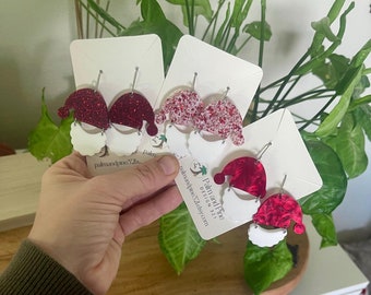 May include: Three pairs of red and white glitter Santa hat earrings on white cards with the text "Palm and Pine Design Etsy.com".