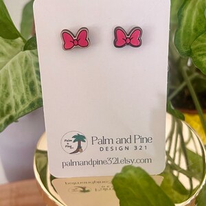 May include: A pair of pink wooden bow earrings on a white card with the text "Palm and Pine DESIGN 321 palmandpine321.etsy.com".