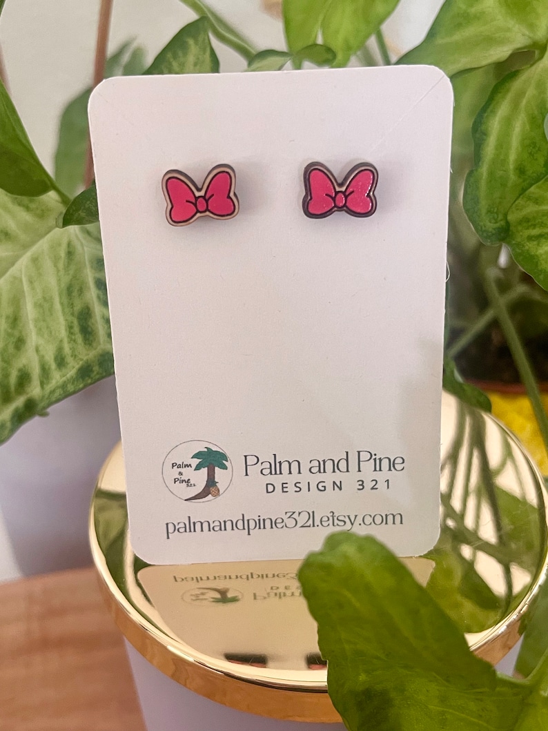 May include: A pair of pink wooden bow earrings on a white card with the text "Palm and Pine DESIGN 321 palmandpine321.etsy.com".