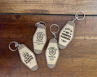 May include: Four wooden keychains shaped like hotel room keys. Each keychain features a different design, including "Keys to My Haunted Mansion", "Tower of Terror", and "Tower of Terror Room 1313".