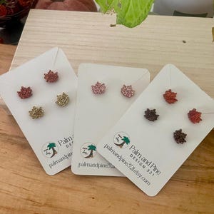 May include: Three cards with pairs of small, sparkly, fall leaf-shaped earrings. The cards are white with a logo that says "Palm and Pine Design 321 palm and pine 321 etsy.com".