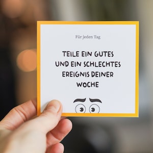 May include: A yellow and white card with the text "F&uuml;r jeden Tag" and "TEILE EIN GUTES UND EIN SCHLECHTES EREIGNIS DEINER WOCHE". The card has a cartoon face with eyebrows and eyes.