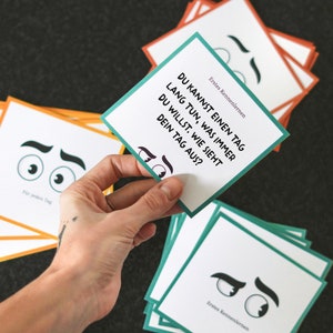 May include: A stack of cards with a green and white card on top. The card has the text "DU KANNST EINEN TAG LANG TUN, WAS IMMER DU WILLST. WIE SIEHT DEIN TAG AUS?" and the text "Erstes Kennenlernen".