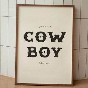 May include: A framed print with the text "you're a COWBOY like me" in a black serif font on a cream background.