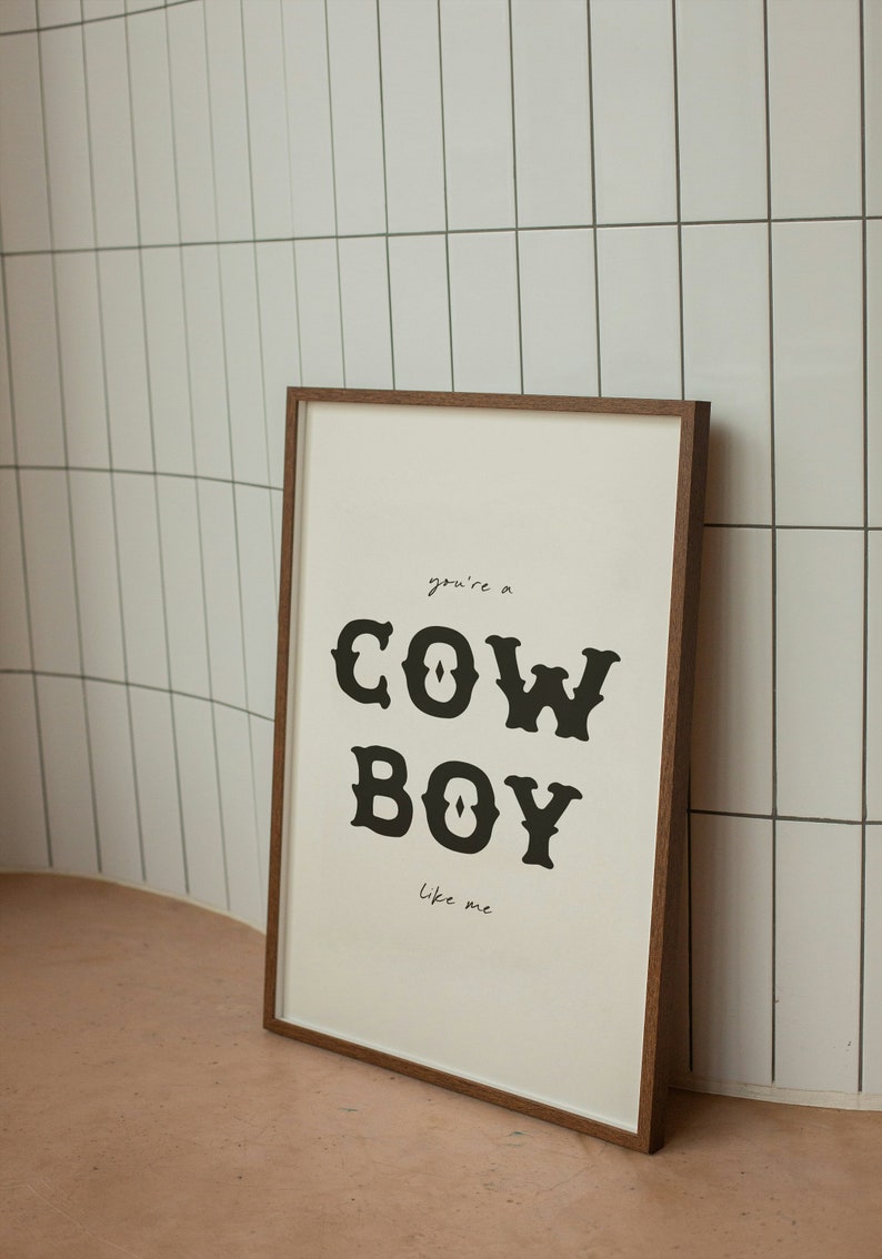 May include: A framed print with a white background and black text that reads "you're a COWBOY like me". The print is in a brown wooden frame.