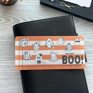 May include: A black leather planner with a decorative card featuring ghost illustrations and the text "BOO!". The card has orange and white stripes and the words "get it DONE" are also visible.