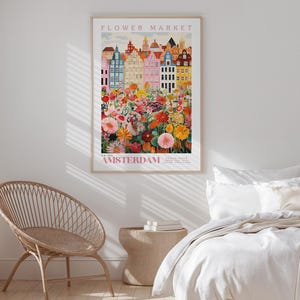a bedroom with a wicker chair, a bed with white bedding, and a poster of a colorful cityscape of Amsterdam hanging on the wall.