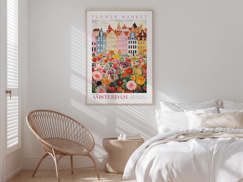 a bedroom with a wicker chair, a bed with white bedding, and a poster of a colorful cityscape of Amsterdam hanging on the wall.
