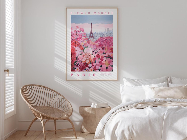 a bedroom with a large poster of a flower market in Paris hanging on the wall. The poster depicts a vibrant scene of pink and red flowers, with the Eiffel Tower visible in the background. The bedroom has a bed with white linens and a wicker chair, creating a cozy and inviting atmosphere.