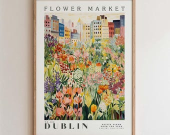 Pode incluir: Uma impressão de arte emoldurada intitulada "Flower Market", apresentando uma ilustração colorida de um campo de flores em frente a um horizonte urbano. A impressão inclui a palavra "Dublin" e a frase "Petite Fleur Pour Tes Yeux". A obra de arte está em uma moldura de madeira.