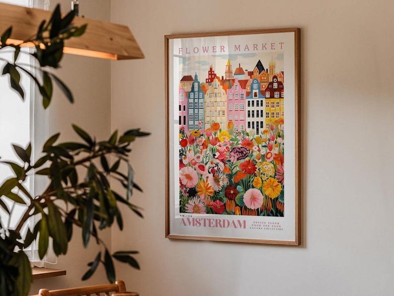 a framed poster of a colorful cityscape with flowers, hanging on a wall in a room with a plant in the foreground.
