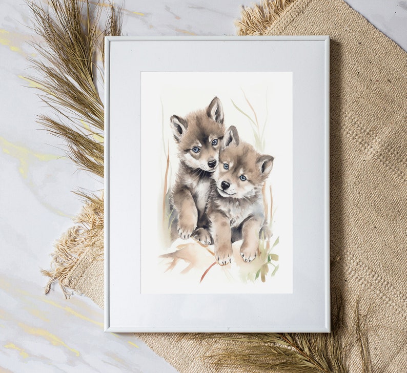 Op de afbeelding: Een aquarel schilderij van twee wolf pups die knuffelen. De pups zijn bruin en grijs met witte markeringen. Het schilderij is tegen een witte achtergrond met een lichtbruine lijst geplaatst.
