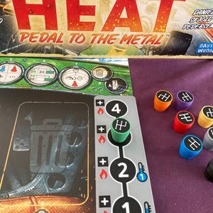 Puede incluir: Primer plano de un tablero de juego con un diseño verde y negro. El tablero presenta una variedad de indicadores y diales. El juego se llama "Heat: Pedal to the Metal". También hay varias piezas de juego de colores con la letra "H" en ellas.